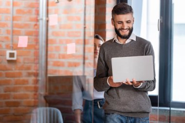 Cam kapı ve iş kadını yakınında dizüstü bilgisayar kullanan neşeli işadamlarının seçici odağı 