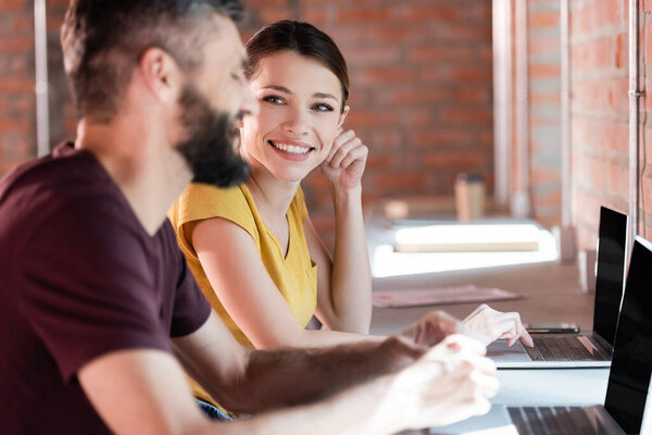 selective focus of happy businesswoman looking at businessman near laptops in office