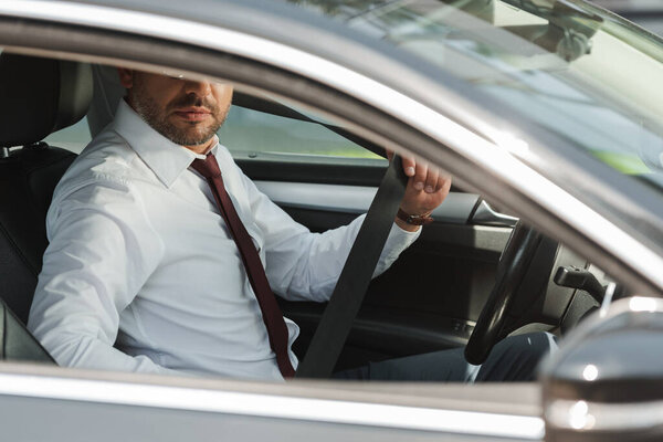 Selective focus of businessman holding seat belt in car 