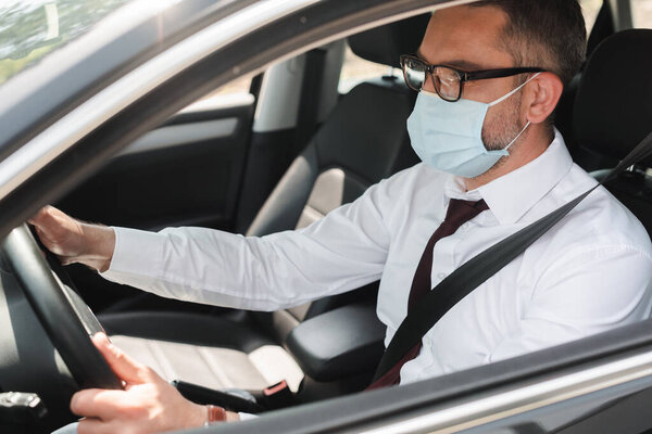 Selective focus of businessman in medical mask driving car 