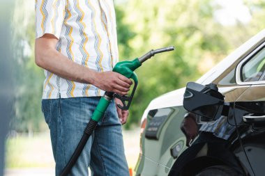 Cropped view of man holding fueling nozzle near car with open gas tank cover outdoors clipart