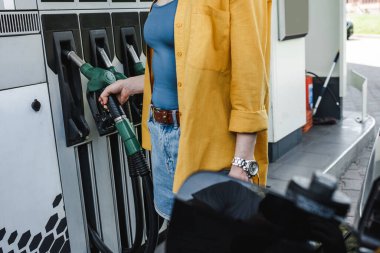 Kentsel caddedeki benzin istasyonunda yakıt pompası alan bir kadının görüntüsü. 