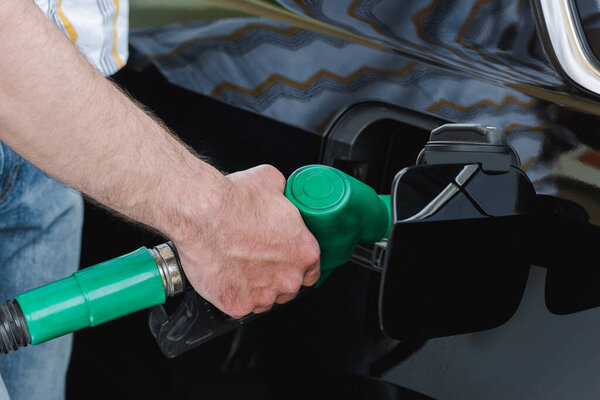 Cropped view of man holding nozzle while fueling car outdoors