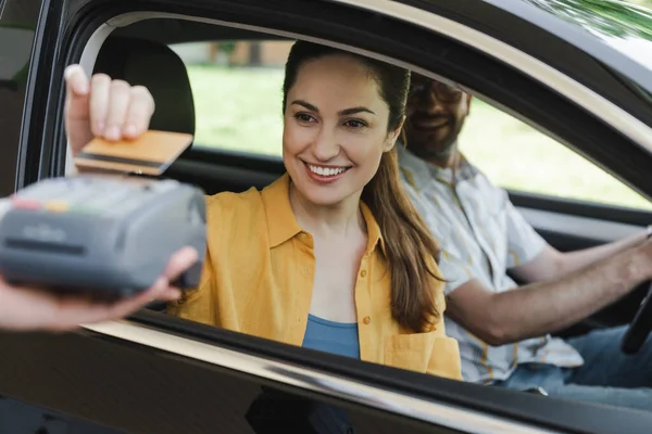 汽车上笑着用信用卡支付近于丈夫的女性和持有支付终端的加油站员工的选择性关注 — 图库照片