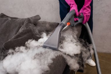 Koltukta sıcak buharlı elektrikli süpürge kullanan lastik eldivenli temizleyici manzarası. 