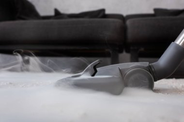 Halıda sıcak buhar olan elektrikli süpürgenin düşük açılı görüntüsü 
