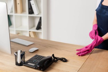 Bilgisayarın yanında lastik eldiven ve ofis masasının üstünde telefon.  