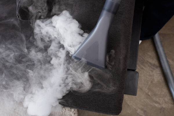 Top view of vacuum cleaner with hot steam on couch 