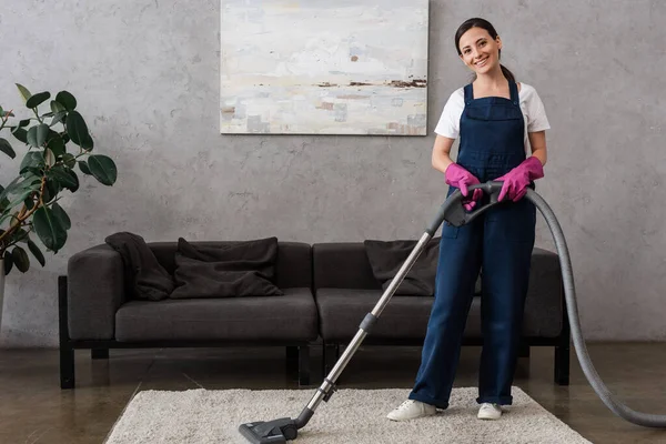 Smiling Cleaner Dalam Seragam Melihat Kamera Sambil Menggunakan Vacuum Cleaner — Stok Foto
