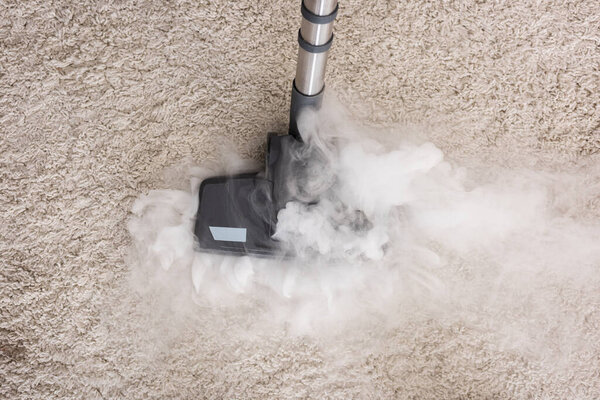 Top view of brush of vacuum cleaner with hot steam on carpet at home 
