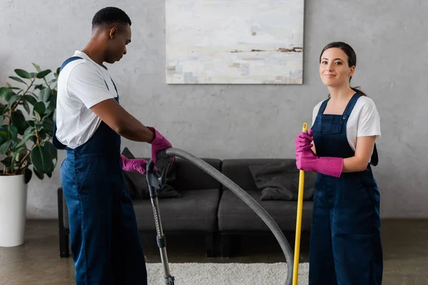 Smiling Cleaner Uniform Looking Camera African American Colleague Vacuum Cleaner — Stock Photo, Image