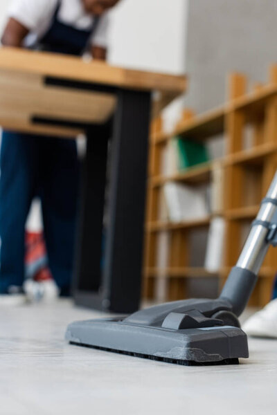 Выборочный фокус щетки пылесоса на полу и африканского американского уборщика в офисе
 