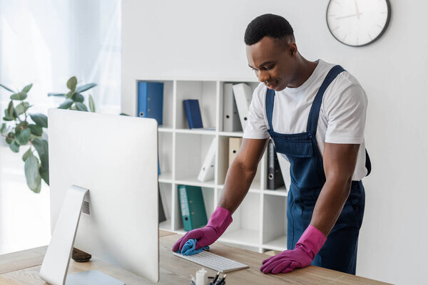 African american worker of cleaning service cleaning computer keyboard with rag in office 