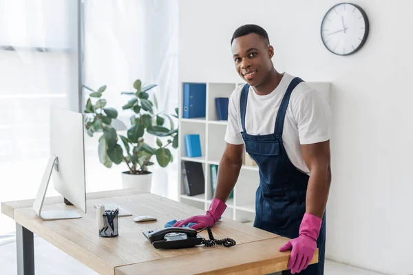 Sorrindo Limpador Americano Africano Com Pano Perto Mesa Escritório — Fotografia de Stock