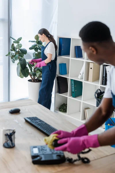 Selective Focus Cleaner Spraying Plant African American Colleague Cleaning Telephone — Stock Photo, Image