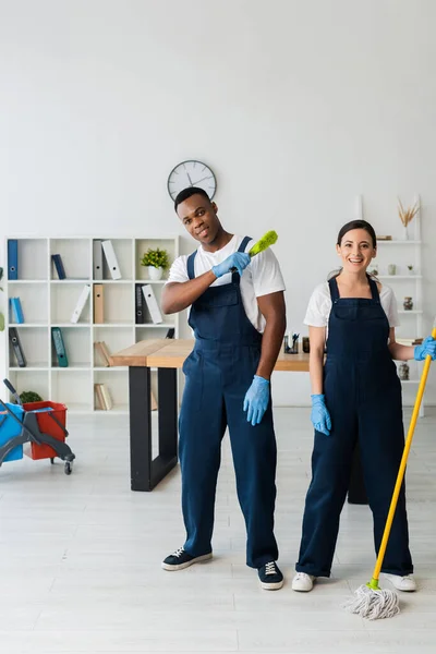 Positive Multiethnic Cleaners Brush Mop Looking Camera Office — Stock Photo, Image