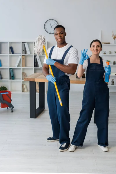 Smiling Multiethnic Cleaners Holding Mop Detergent Showing Gesture Office — Stock Photo, Image