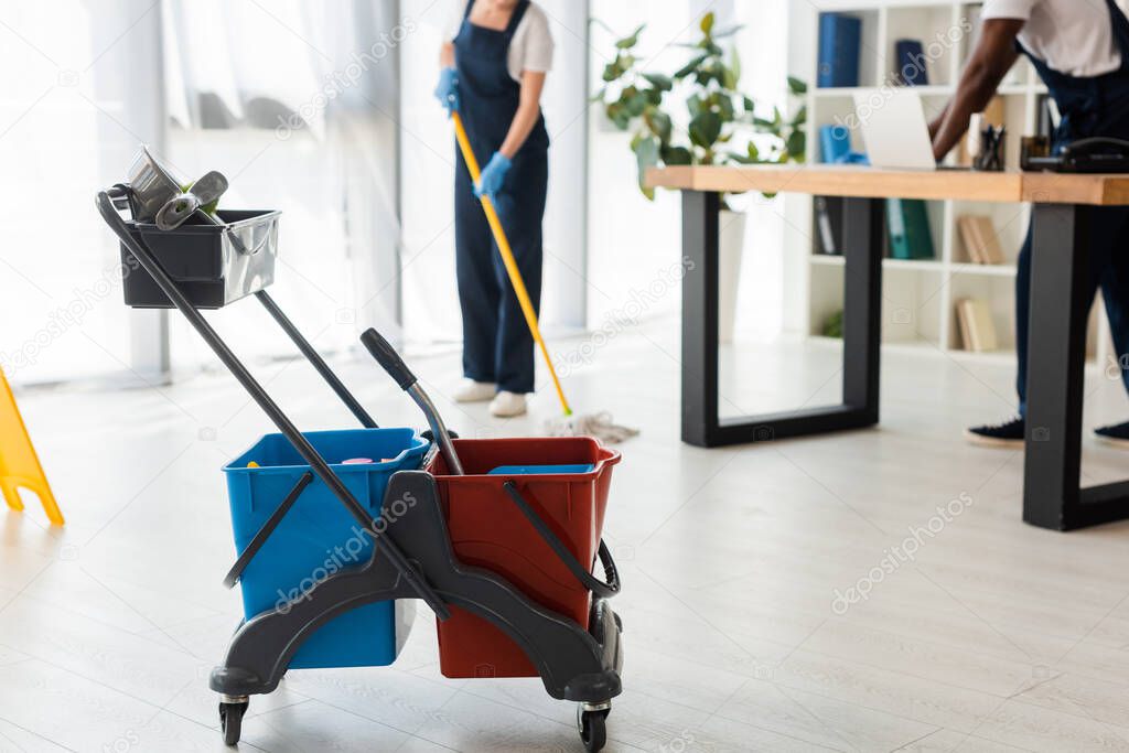 Selective focus of buckets with cleaning supplies and multiethnic cleaners working in office 