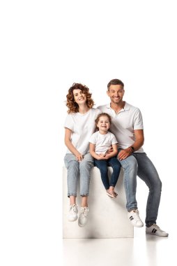 Neşeli aile gülümsüyor ve beyaz küpün üzerinde oturuyor.