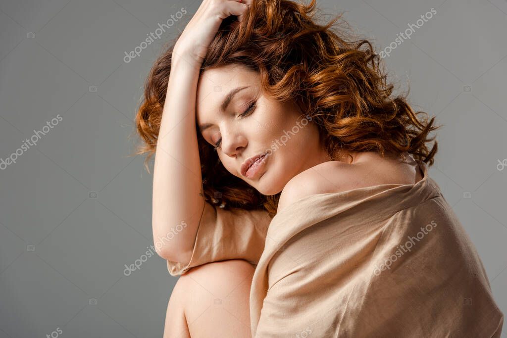 Curly woman with closed eyes touching hair isolated on grey