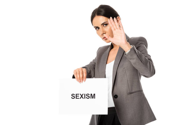 businesswoman showing stop sign while holding placard with sexism lettering isolated on white