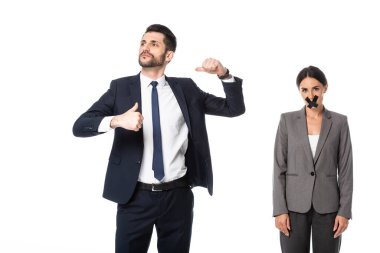 arrogant businessman in suit pointing with thumbs at himself near woman with scotch tape on mouth isolated on white clipart