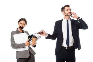 İş adamı, sekreterin yanında, ağzında bant, kağıt bardak ve beyaz ellerindeki klasörlerle konuşuyor.