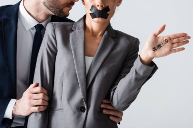cropped view of businessman molesting businesswoman with scotch tape on mouth showing hand with me too lettering isolated on white clipart