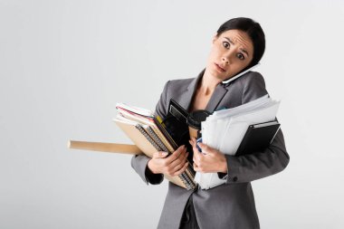 Elinde hesap makinesi, kağıt bardak, belgeler, klasörler ve defterler tutan meşgul bir iş kadını beyaz telefonda konuşurken 