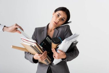 busy businesswoman holding calculator, paper cup, documents, folders and notebooks while talking on smartphone near businessman isolated on white  clipart