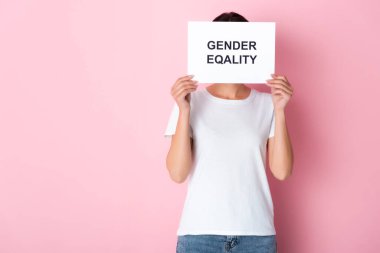 woman in white t-shirt covering face with gender equality lettering on placard and standing on pink  clipart