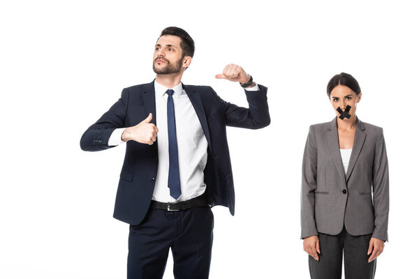 arrogant businessman in suit pointing with thumbs at himself near woman with scotch tape on mouth isolated on white