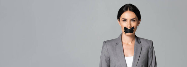 panoramic orientation of businesswoman with scotch tape on mouth isolated on grey