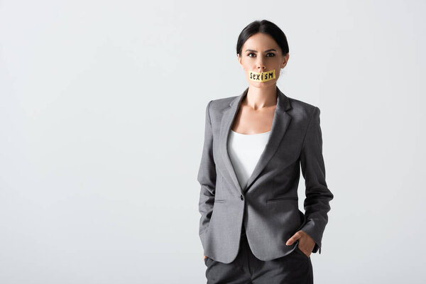 businesswoman with sexism lettering on duct tape standing with hands in pockets isolated on white 