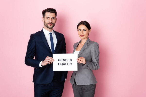 handsome businessman and businesswoman holding placard with gender equality lettering on pink 
