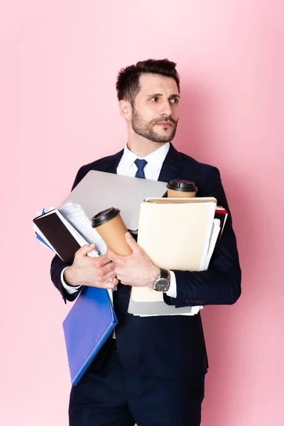 Przystojny Biznesmen Trzymając Papierowe Kubki Laptop Teczki Notatniki Patrząc Różowy — Zdjęcie stockowe