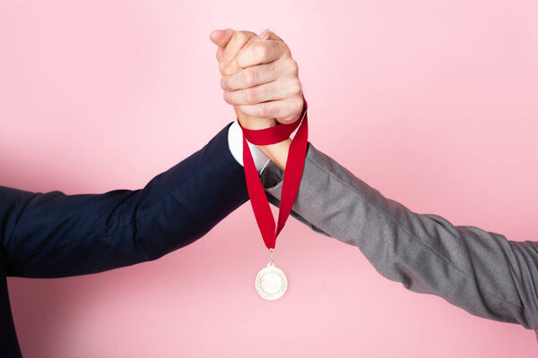 cropped view of businessman and businesswoman holding hands and golden medal on pink, gender equality concept