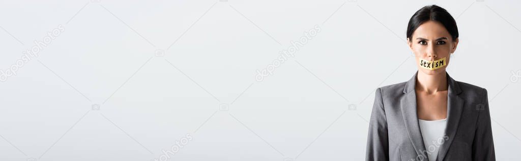 panoramic orientation of businesswoman with sexism lettering on duct tape looking at camera isolated on white 