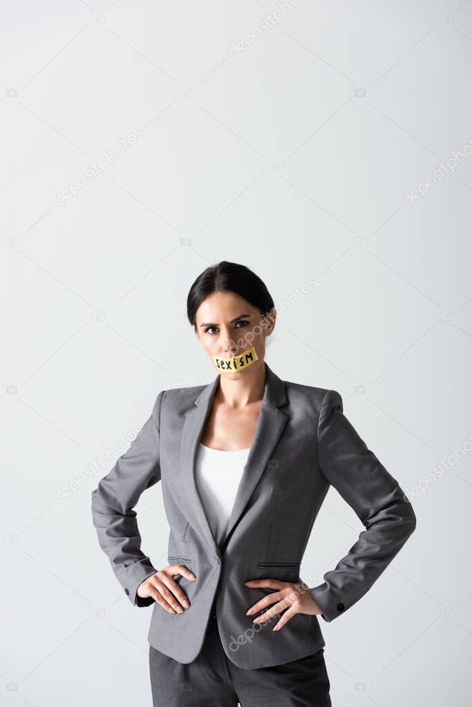 businesswoman with sexism lettering on duct tape standing with hands on hips isolated on white 