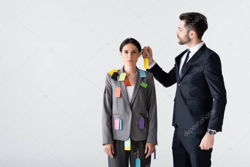 bearded businessman putting label on beautiful businesswoman isolated on white, sexism concept 