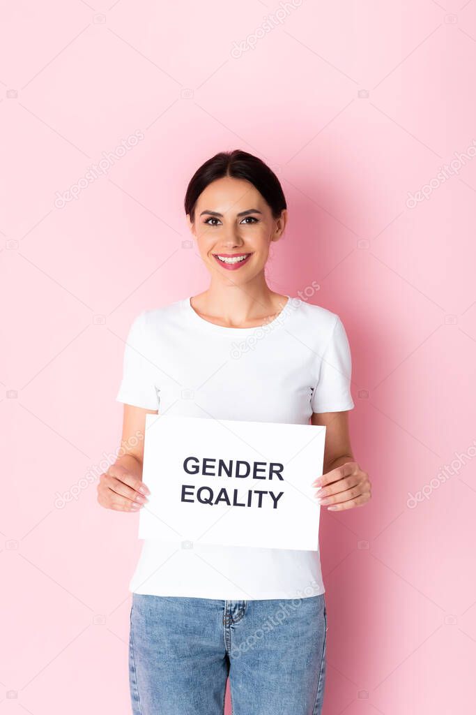 happy woman in white t-shirt holding placard with gender equality lettering on pink 