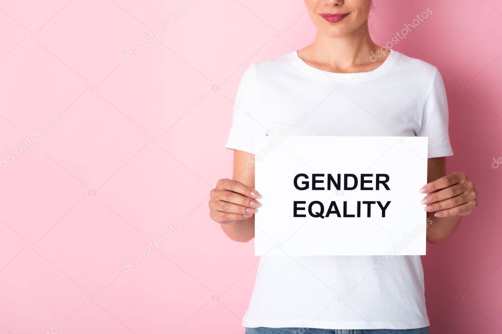 cropped view of woman in white t-shirt holding placard with gender equality lettering on pink 
