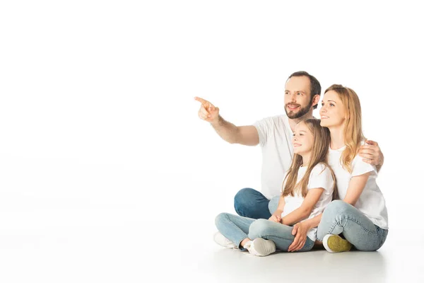 happy family sitting on floor with crossed legs while man pointing away isolated on white