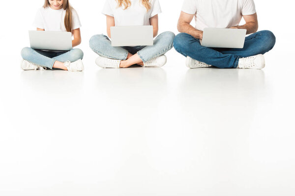обрезанный вид семьи, сидящей на полу с ноутбуками на скрещенных ногах на белом