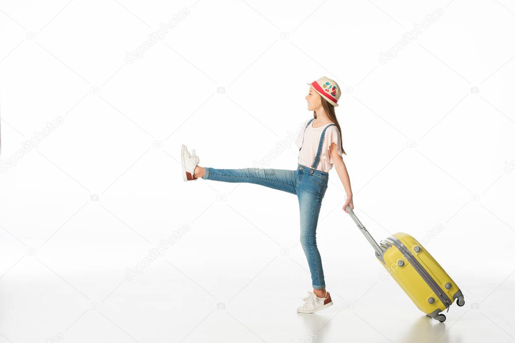 side view of girl in hat marching with yellow travel bag isolated on white