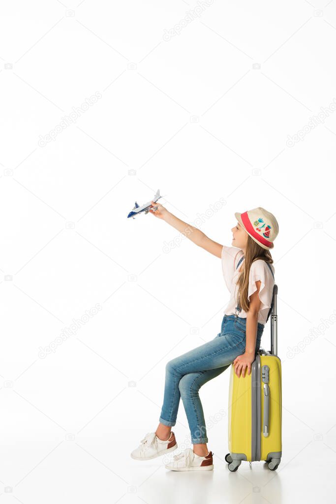 girl in hat with plane model on yellow travel bag isolated on white