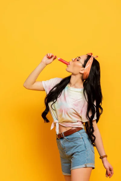 黄色の背景でアイスクリームを食べるスタイリッシュな夏のブルネットの女の子の側面図 — ストック写真