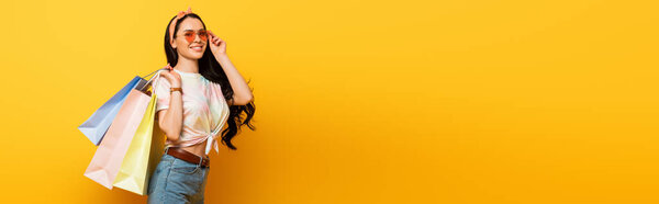 smiling stylish summer brunette girl with shopping bags on yellow background, panoramic shot