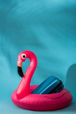 Mavi arka planda pembe şişirilebilir flamingo ve bavul.