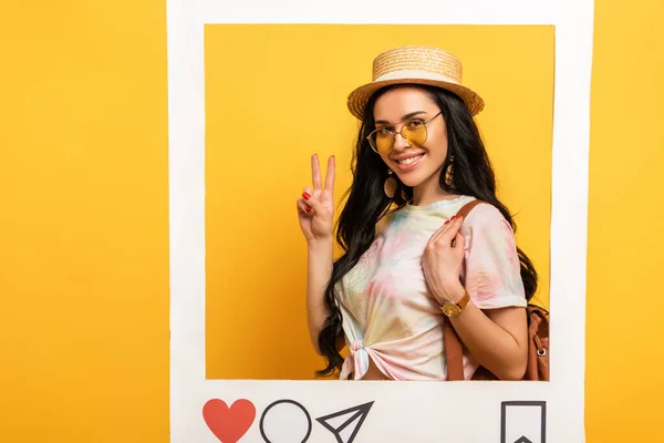 穿着夏装的快乐的黑发女孩在黄色背景的社交网站上展示和平标志 — 图库照片